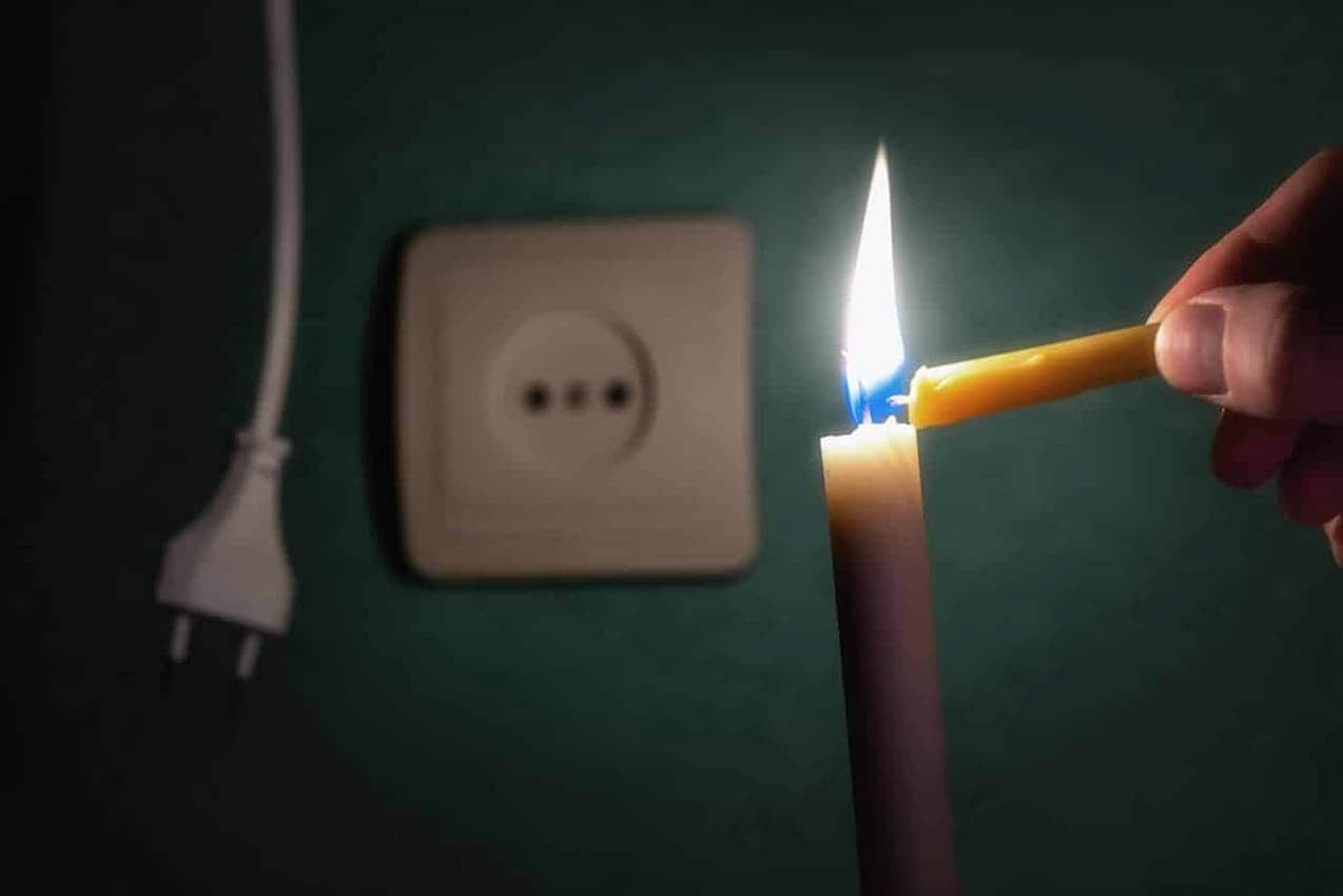 Mão acendendo vela ao lado de uma tomada.