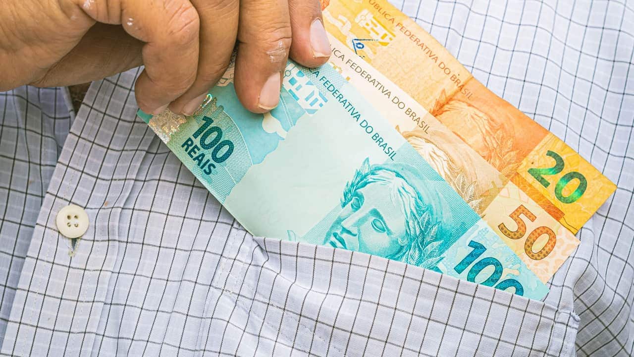 Mão colocando notas de dinheiro no bolso da camisa