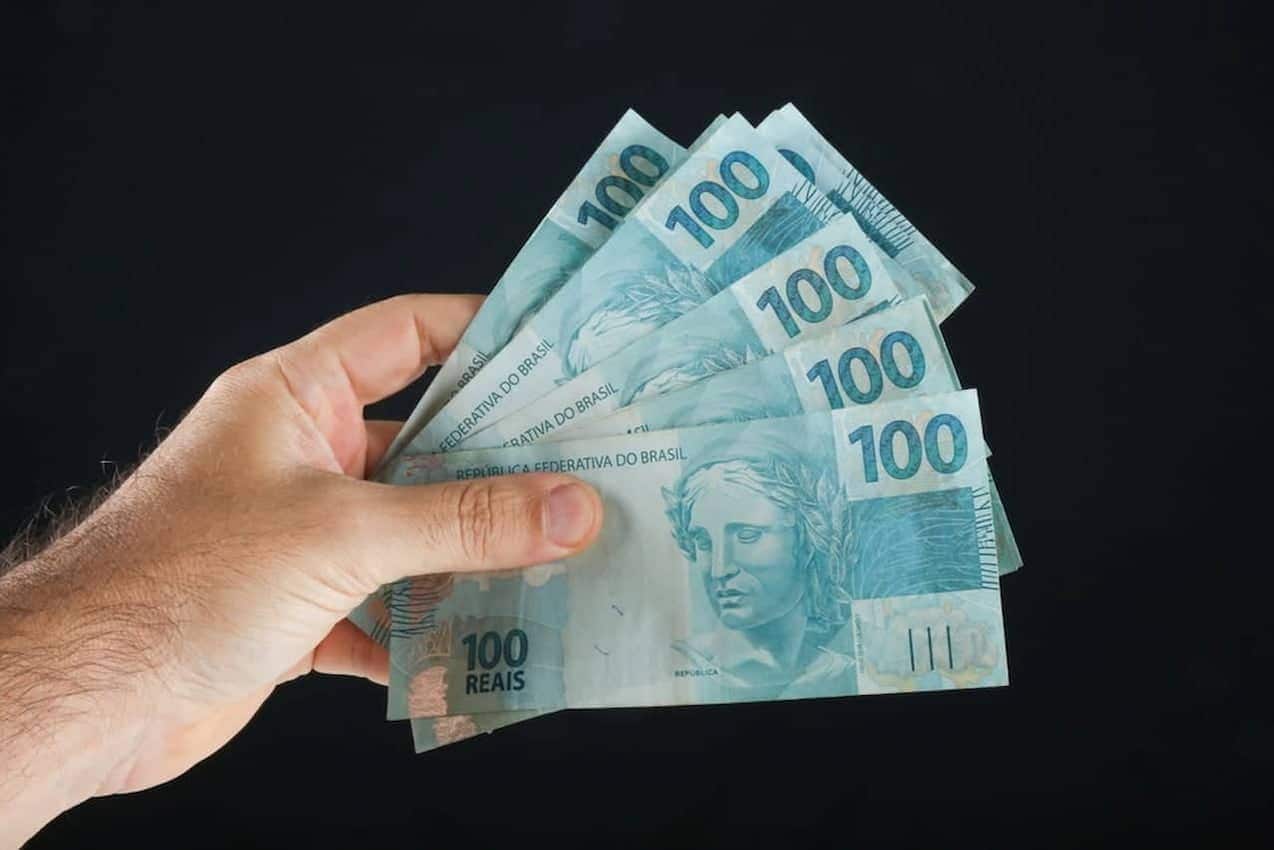 Mão segurando várias notas de 100 reais pagamento