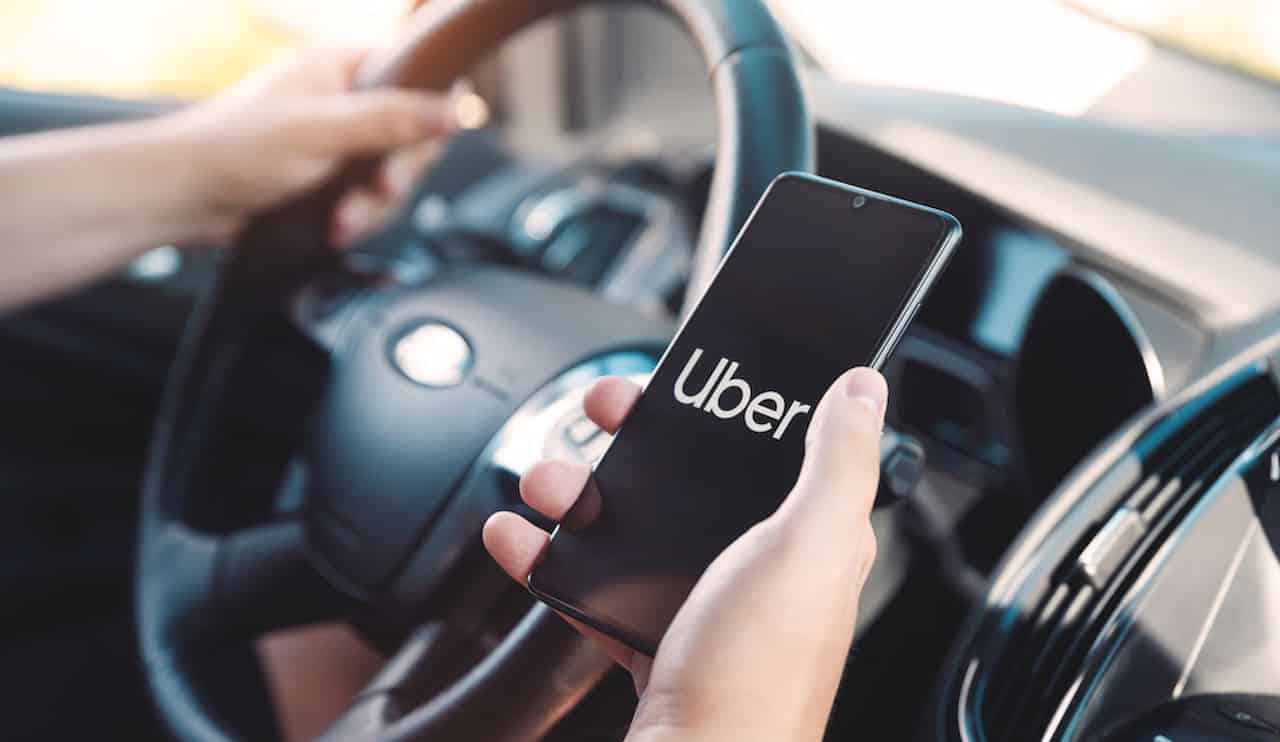 Dentro de um carro, mão segurando celular com logo Uber.