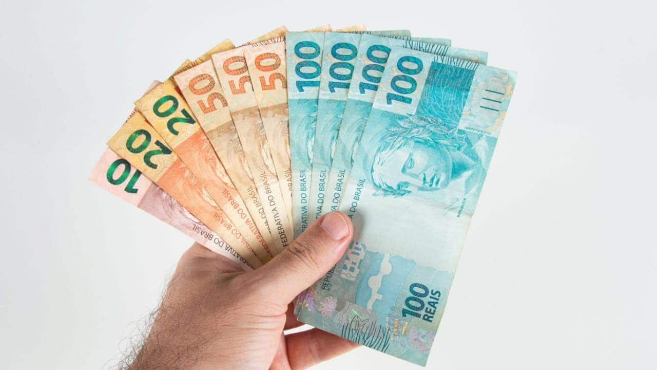 Mão segurando notas de 10, 20, 50 e 100 reais