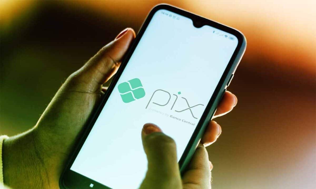 Imagem de uma pessoa segurando o celular com o PIX em nome e em logo.