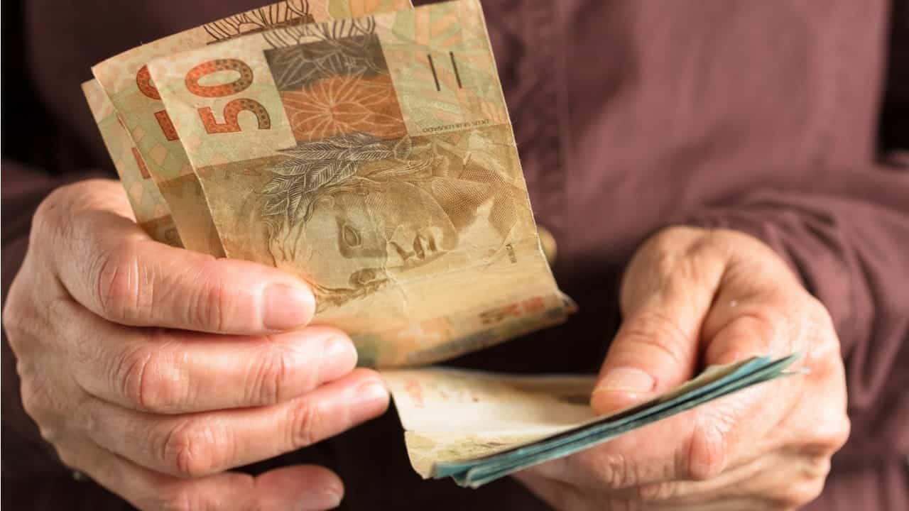 Na imagem, mãos contando notas de cinquenta reais.