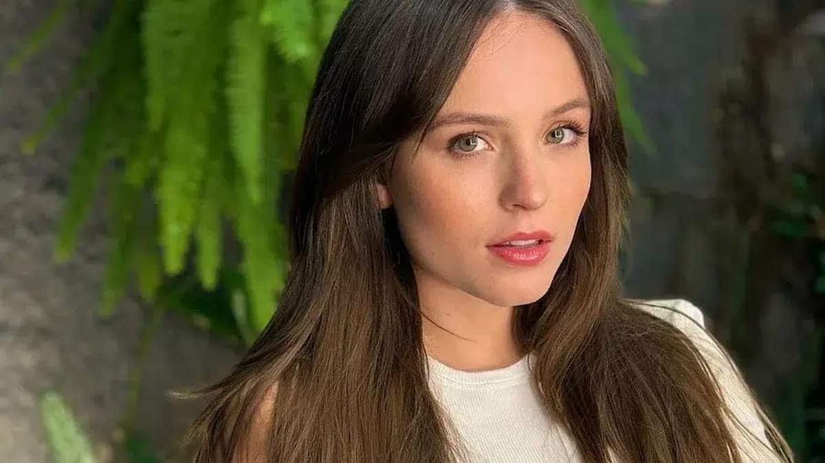 A imagem mostra Larissa Manoela, somente o rosto, com uma blusa branco e um fundo com plantas.