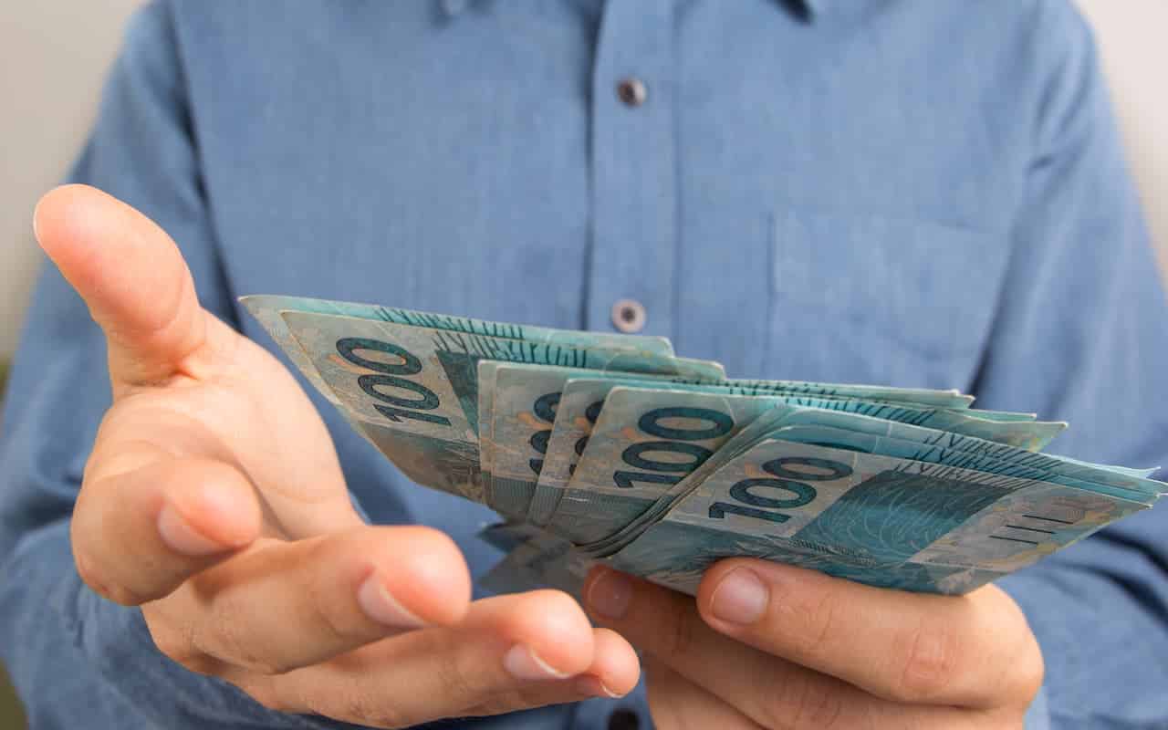 mão oferecendo notas de cem reais