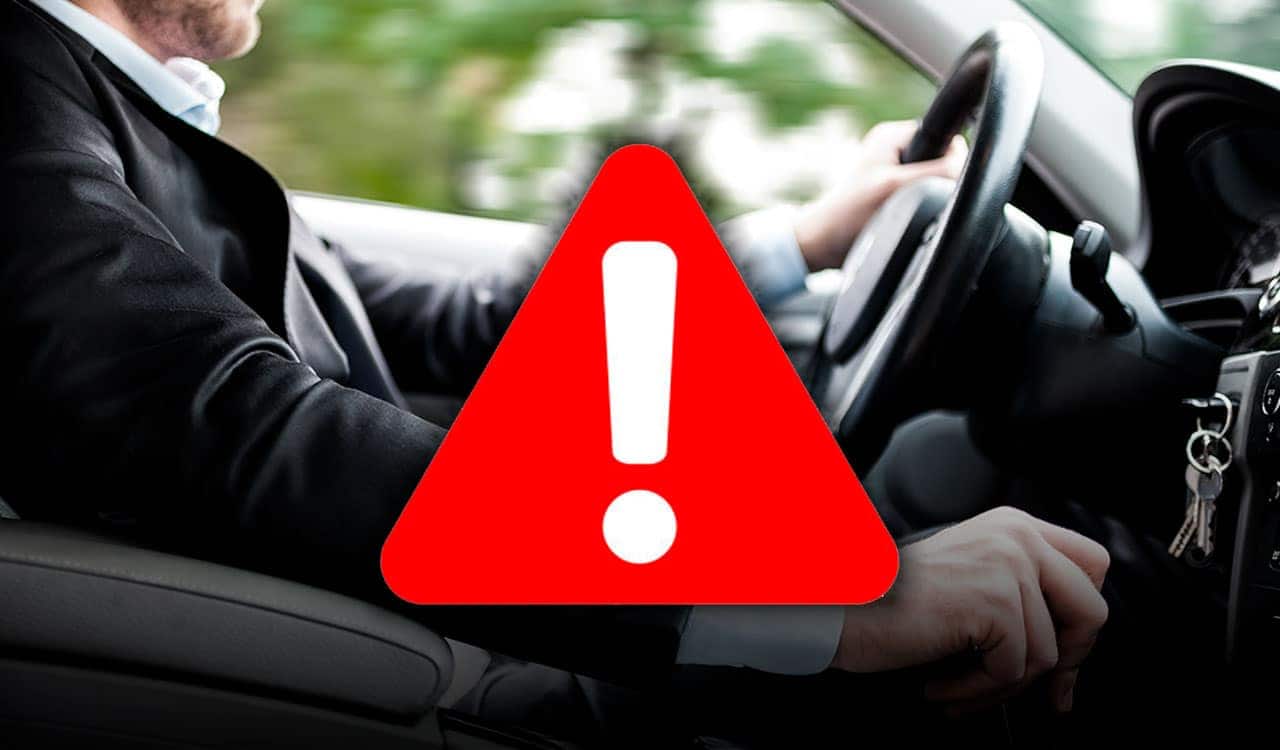 Motorista ao volante e em destaque uma figura com o ponto de exclamação em branco dentro de um triângulo vermelho.