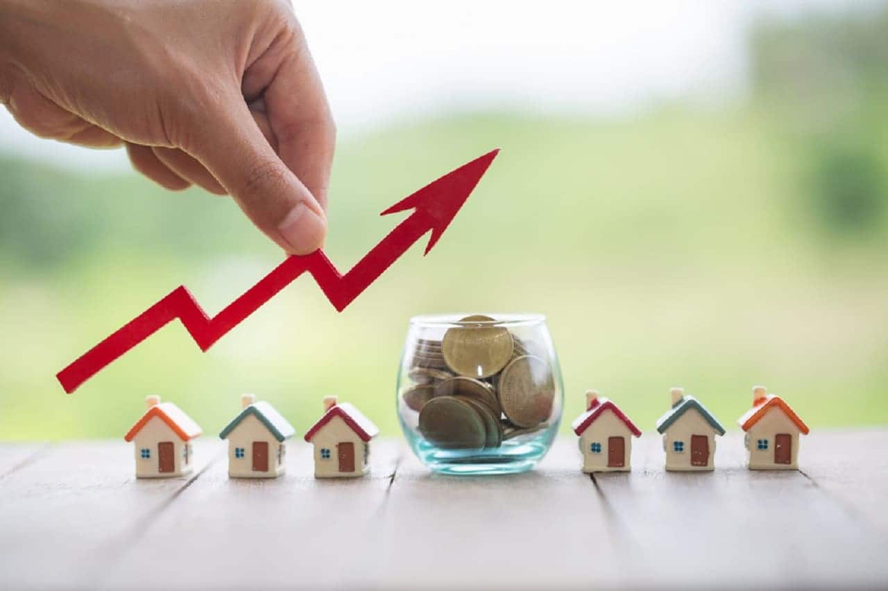 Imagem de uma gráfico de algo ao lado de casas em miniatura e um pote de moedas.
