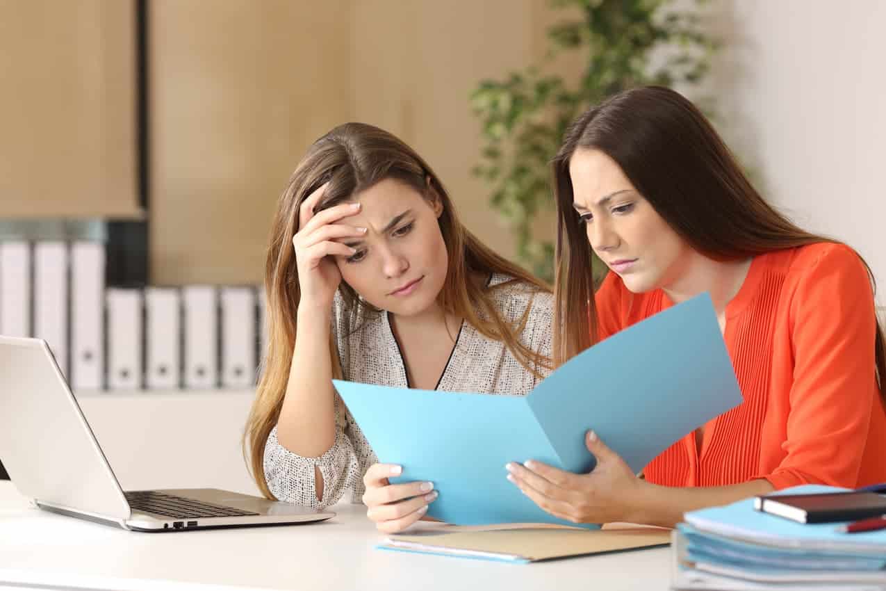 Duas mulheres sentadas, olhando uma planilha, com expressão de preocupação