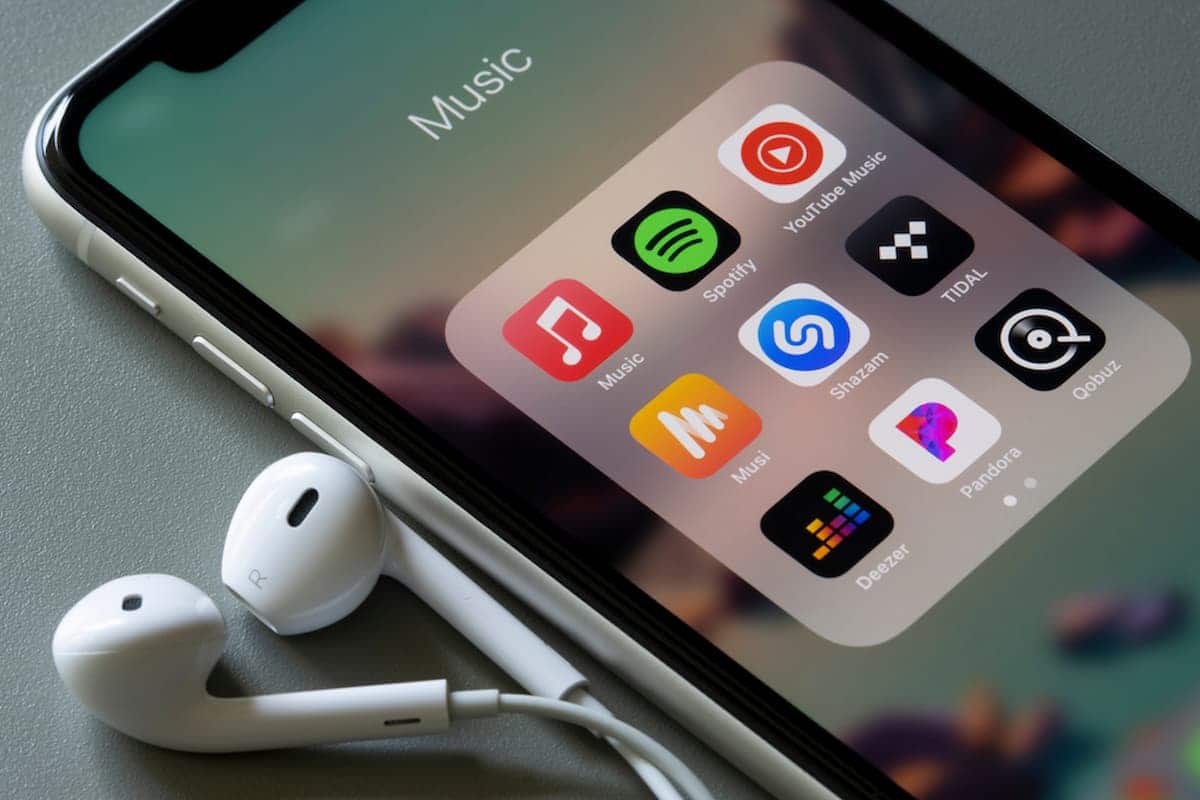 Celular mostrando as principais plataformas de streaming de música com um fonte de ouvido ao lado