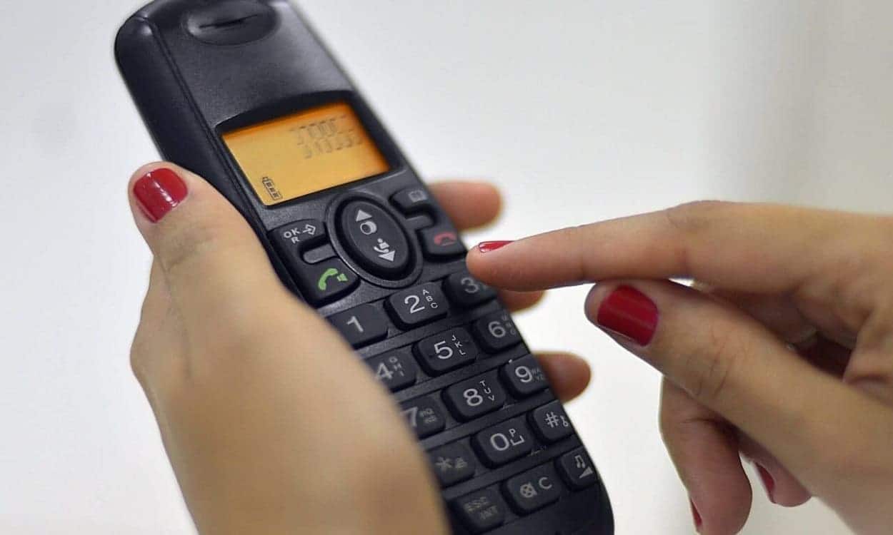 Pessoa discando os números em um aparelho telefônico sem fio