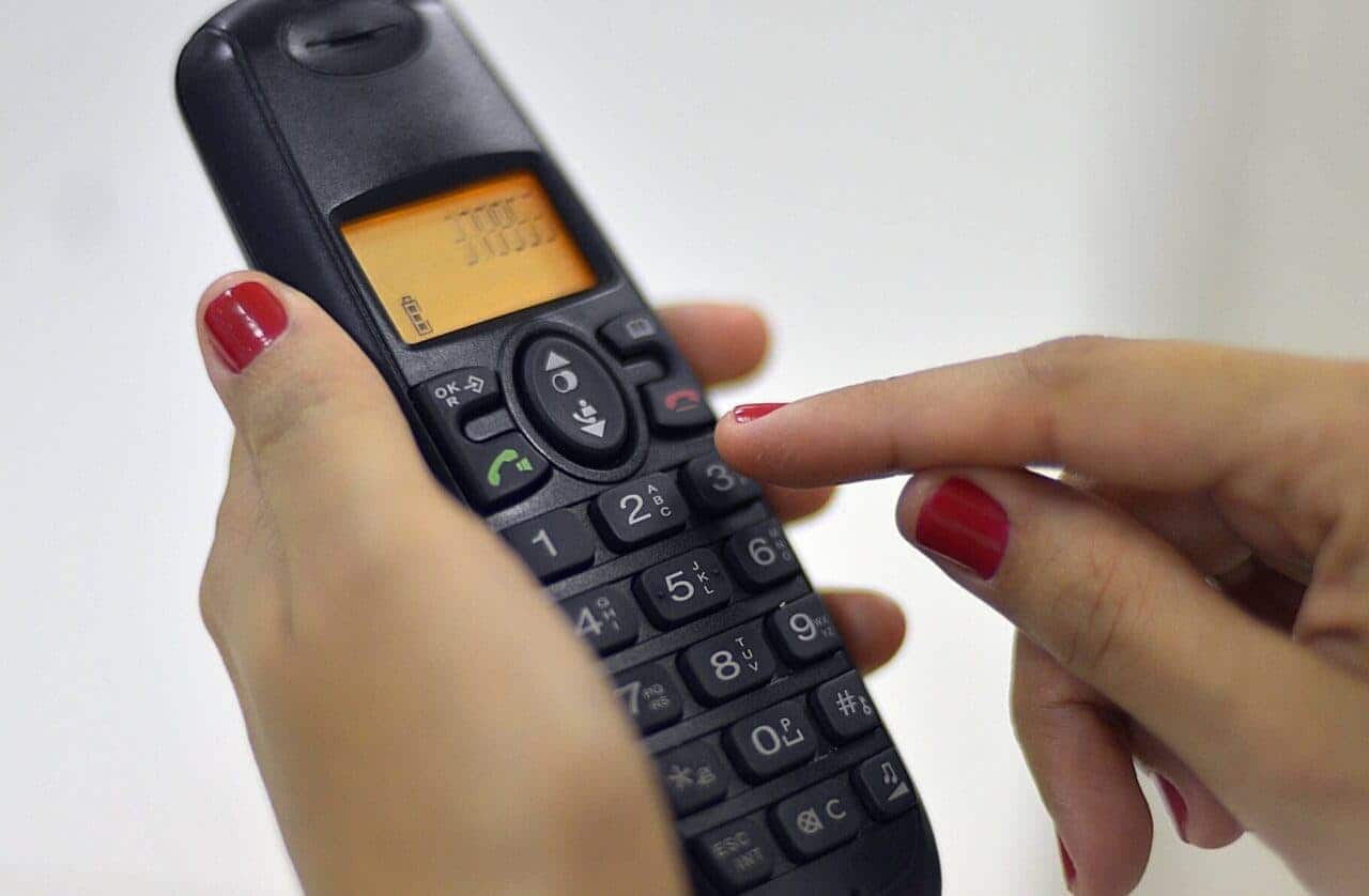 Pessoa discando os números em um aparelho telefônico sem fio
