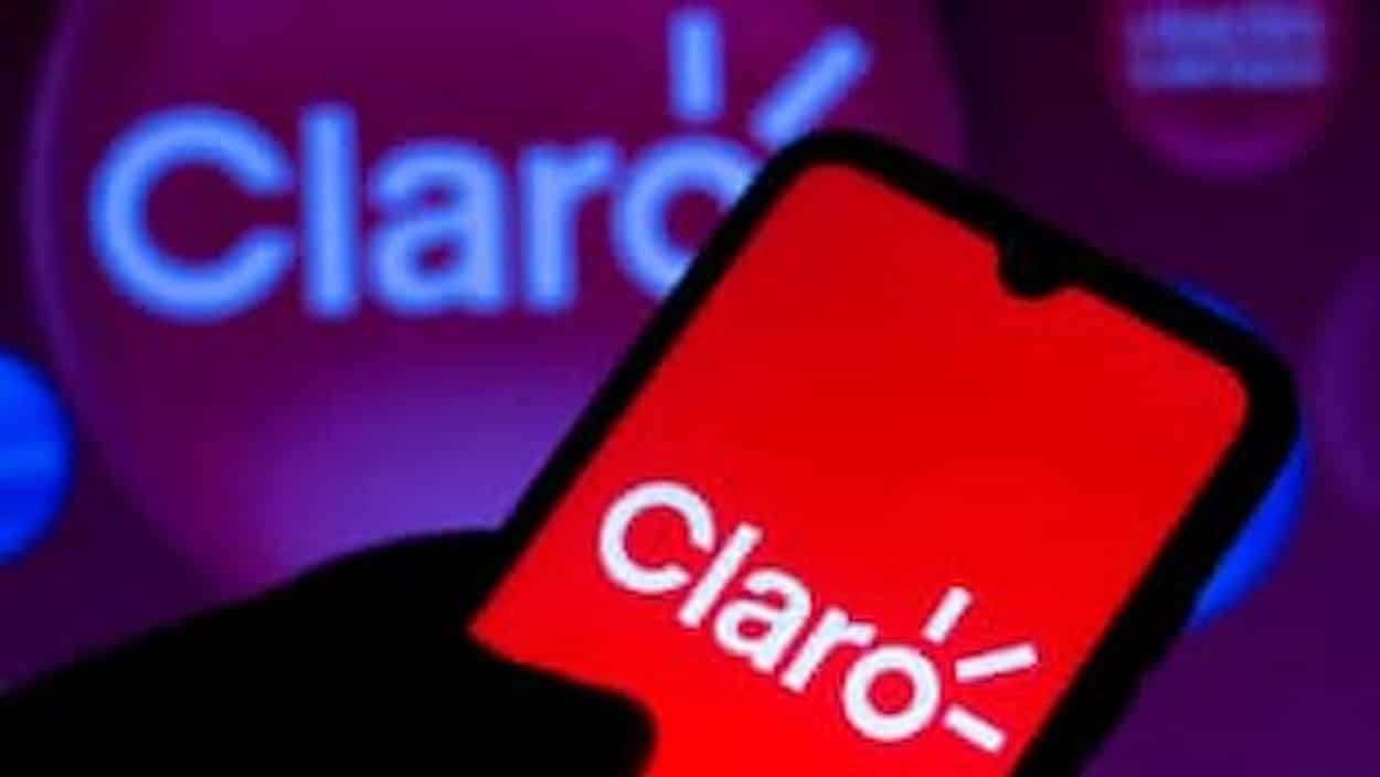 Mão segurando celular exibindo logo da Claro na tela. Ao fundo a logo da Claro também é destacado. celulares