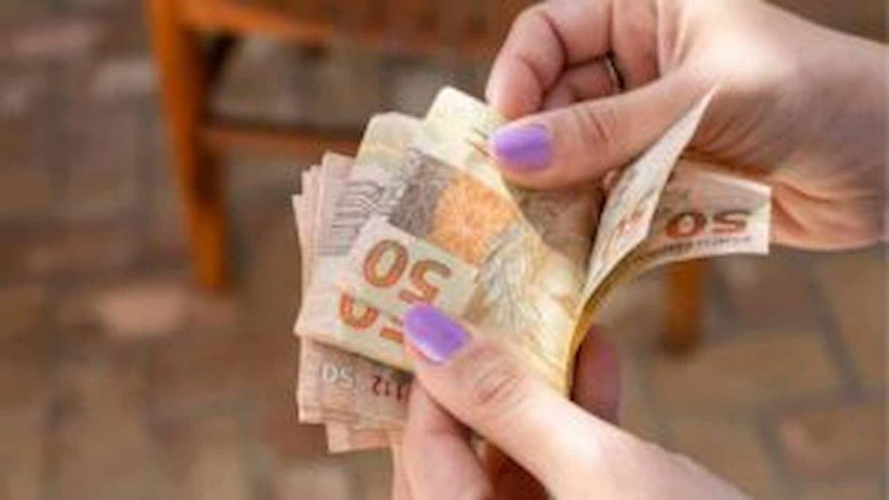 mãos feminina com esmalte rosa nas unhas contando R$ 150 em notas de R$ 50