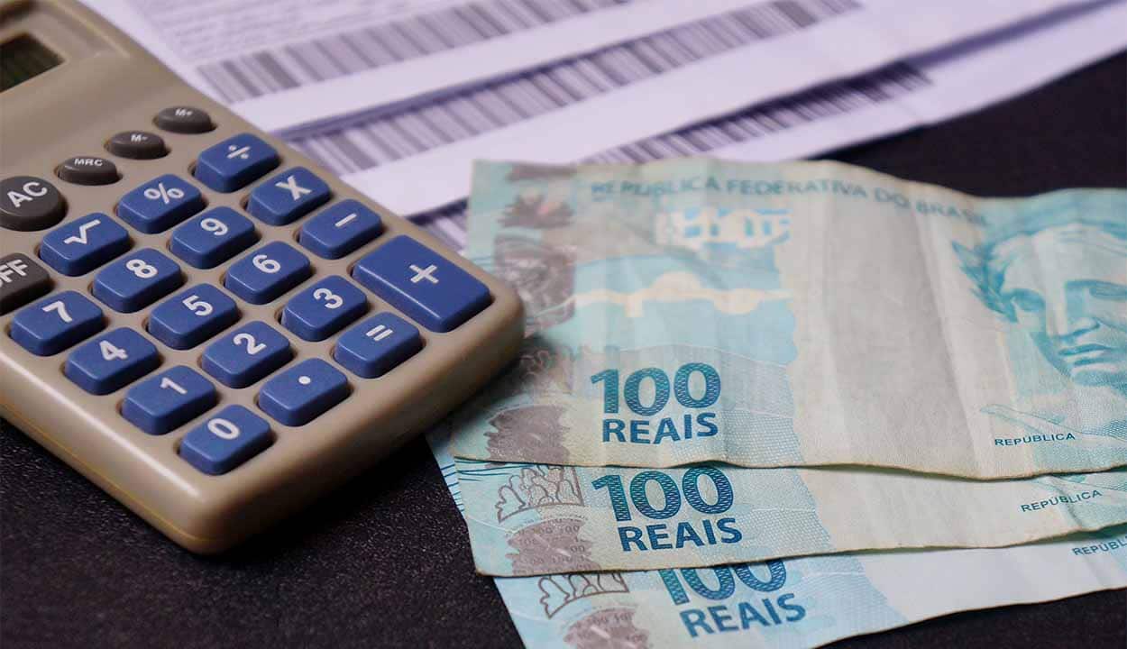 Calculadora com cédulas de 100 reais e um boleto ao lado.