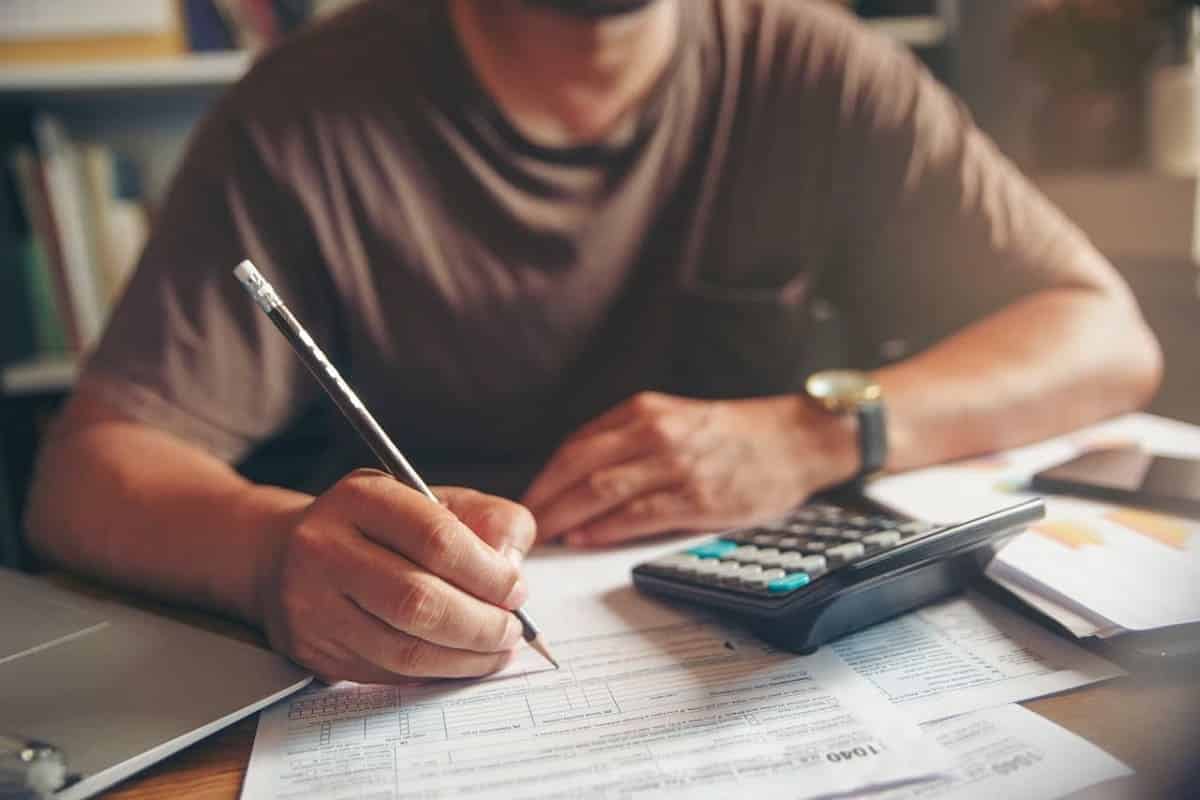 Pessoa escrevendo em papelada de dívidas e calculadora.