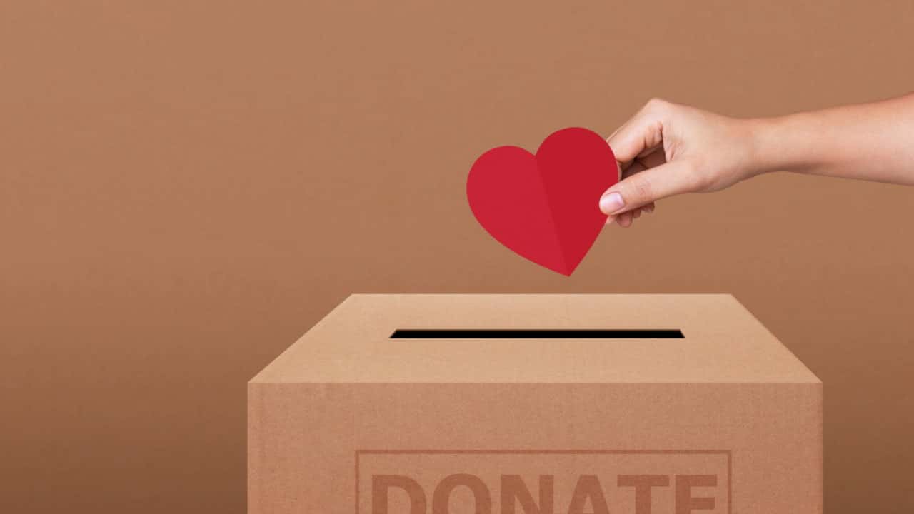 Mão colocando recorte em formato de coração em uma caixa de papelão, simbolizando doação para ONGs