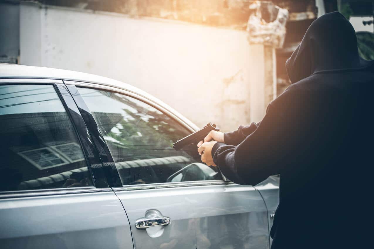 Na imagem, criminoso assaltando carro ao apontar arma para veículo.