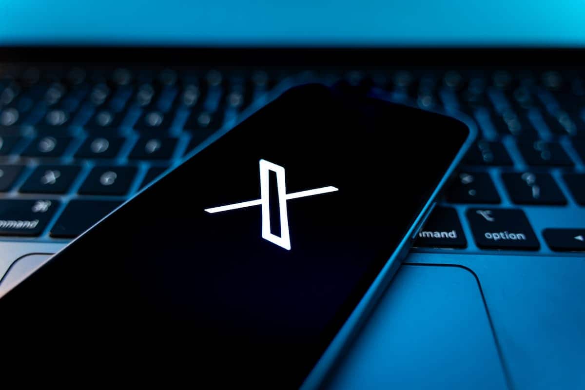 Aplicativo X em celular de usuário da plataforma apoiado sobre teclado de notebook