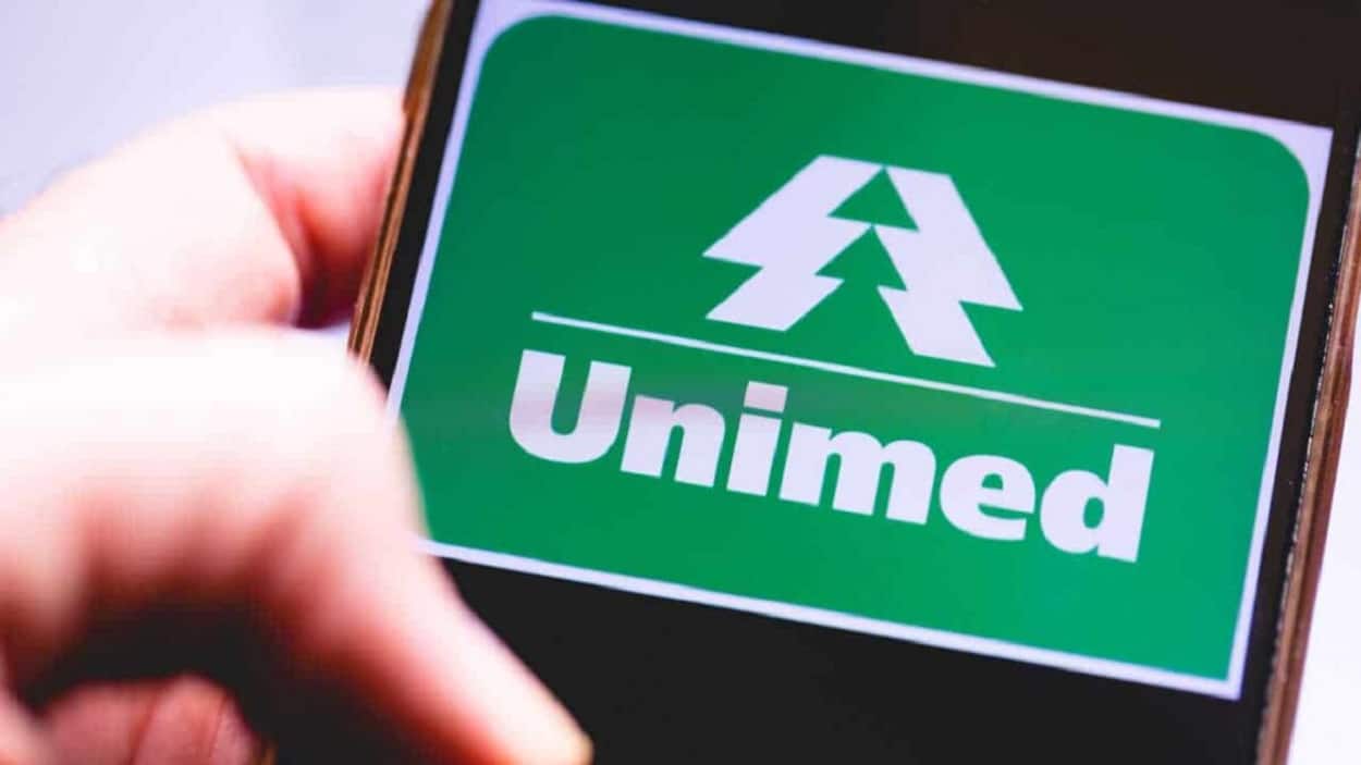 Celular com logo da Unimed exibida na tela. Há um dedo desfocado, em primeiro plano.