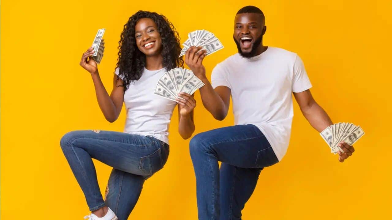Casal com várias notas de dinheiro nas mãos e sorrisos nos rostos.