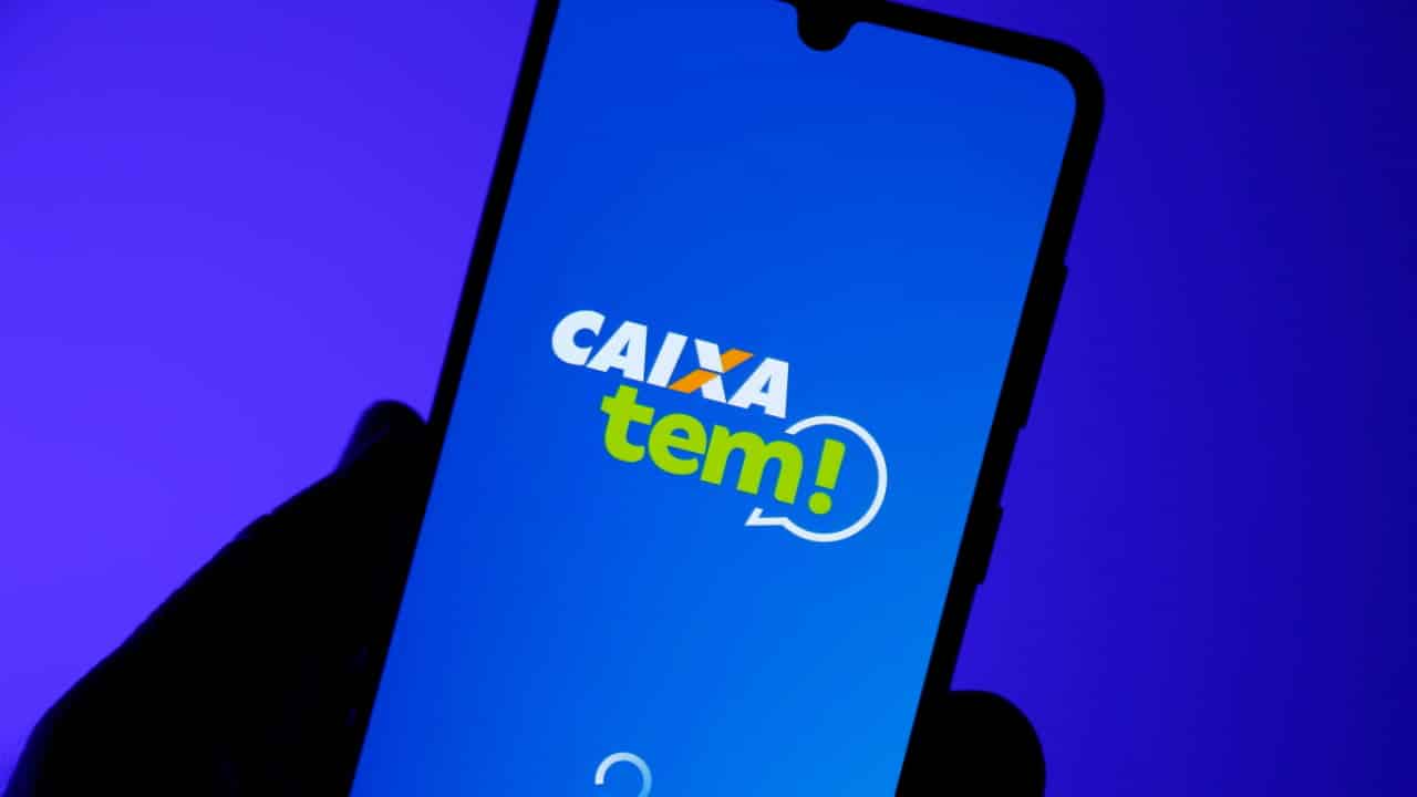Mão segurando celular com tela inicial do app Caixa Tem