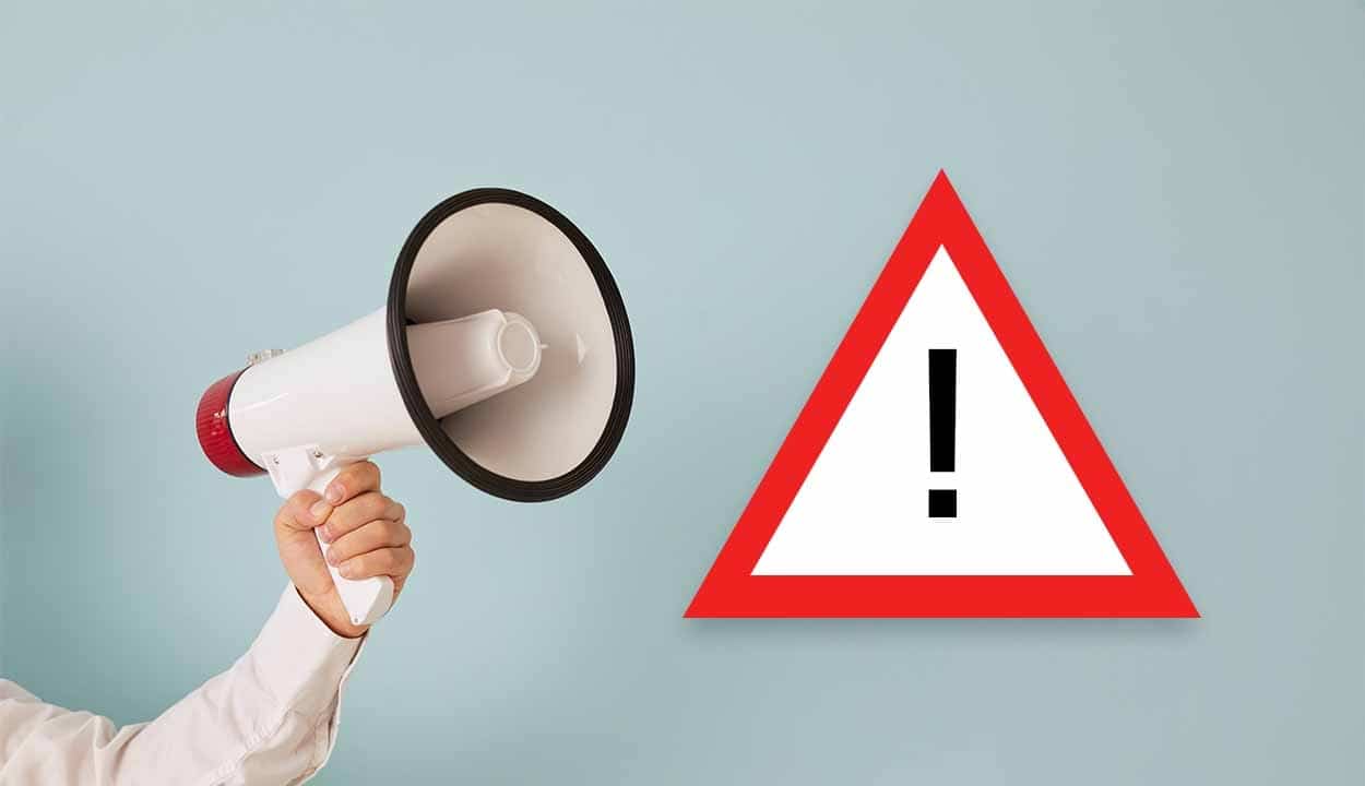 Imagem de uma mão segurando um megafone. Ao lado, uma placa com a exclamação em destaque.