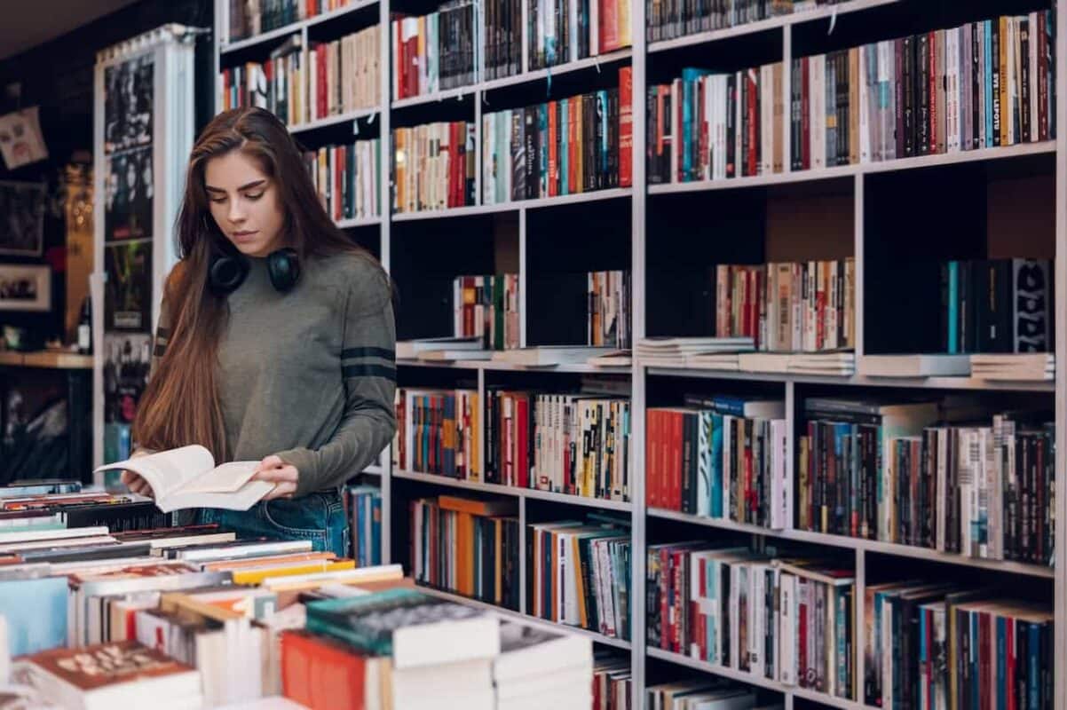 Mulher abrindo livro em uma livraria edital