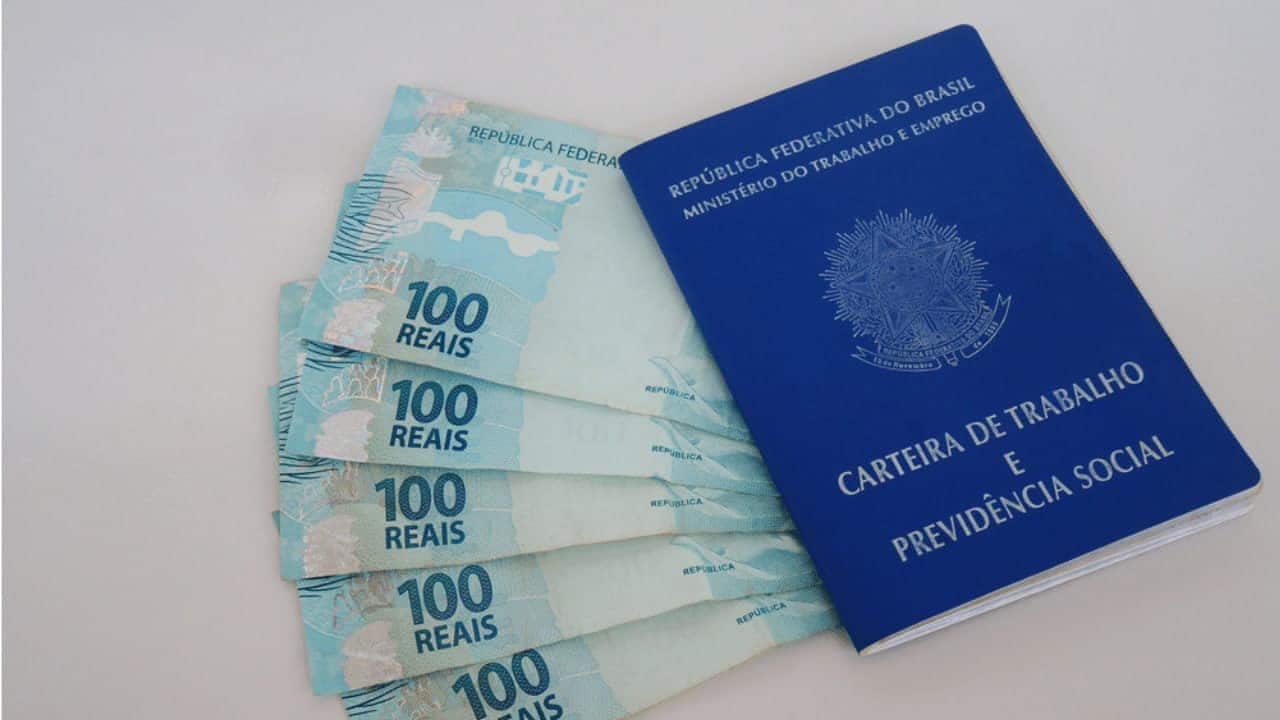 notas de cem reais postas embaixo de uma carteira nacional de trabalho