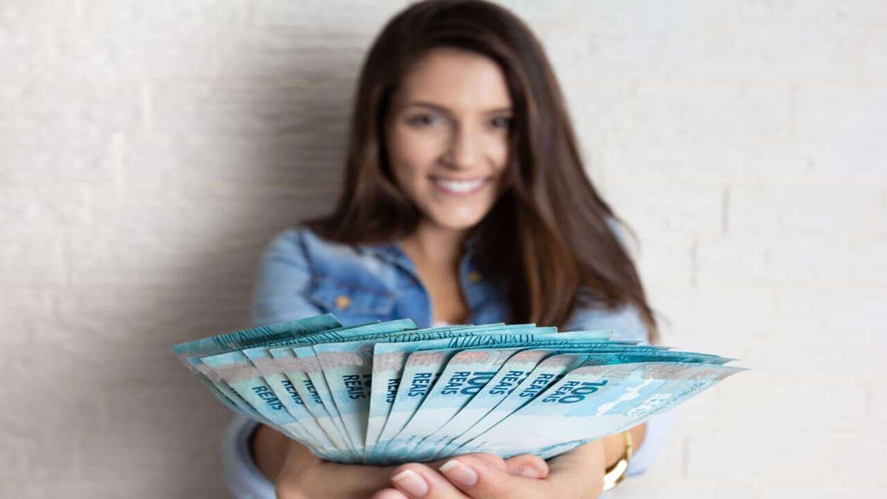 Mulher sorrindo com notas de dinheiro brasileiro