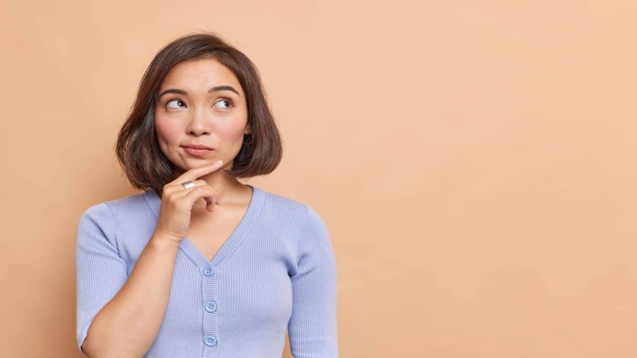 Mulher de descendência asiática com mão no queixo e expressão confusa