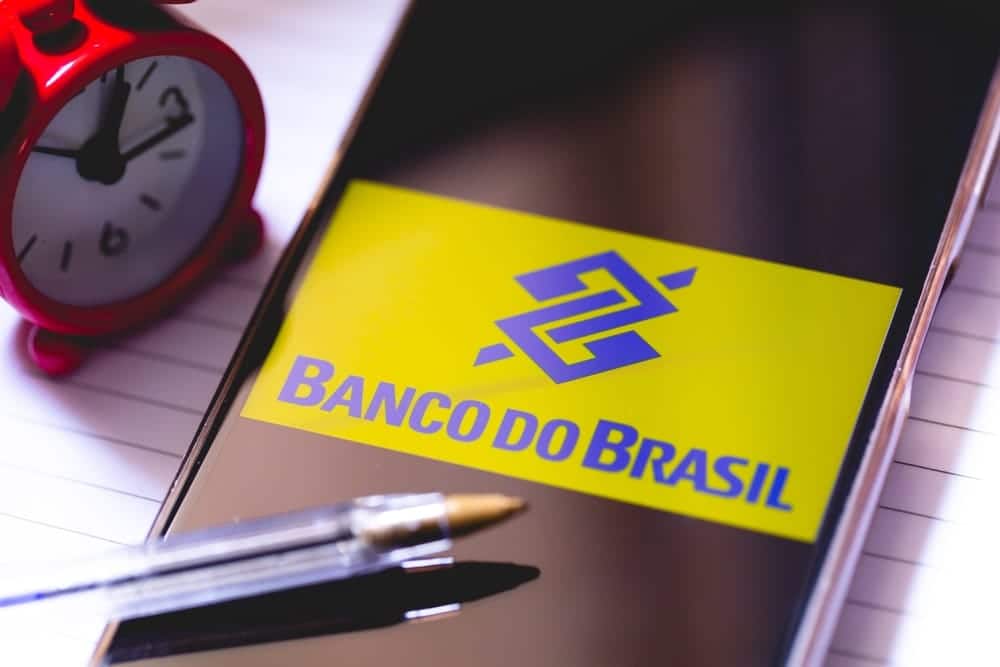 Celular com tela aberta no Banco do Brail, apoiado em caderno, com relógio ao lado