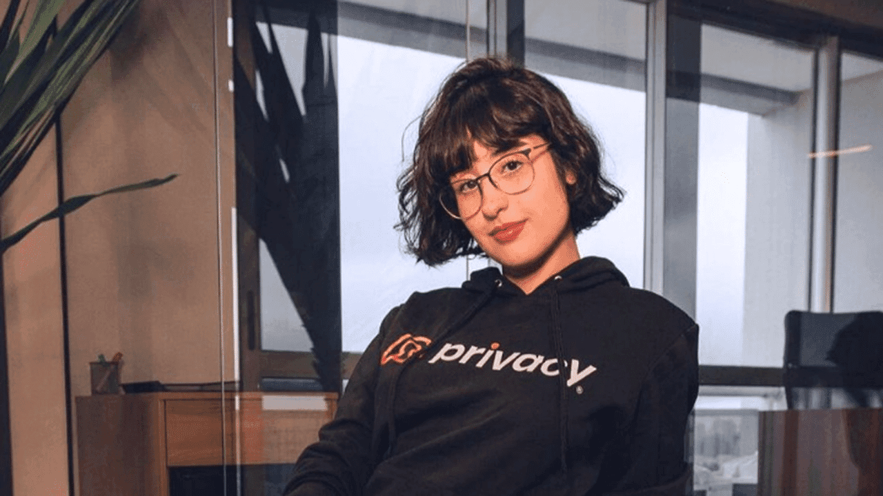 Imagem da modelo Beiçola do Privacy usando uma blusa preta com o logotipo da Privacy. Ela tem abelo curto à altura do pescoço, usa óculos e está de batom vermelho.