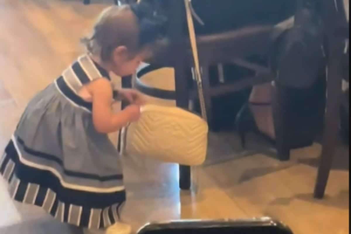 Criança de dois anos com vestido azul abaixada com a mão em bolsa cor de creme