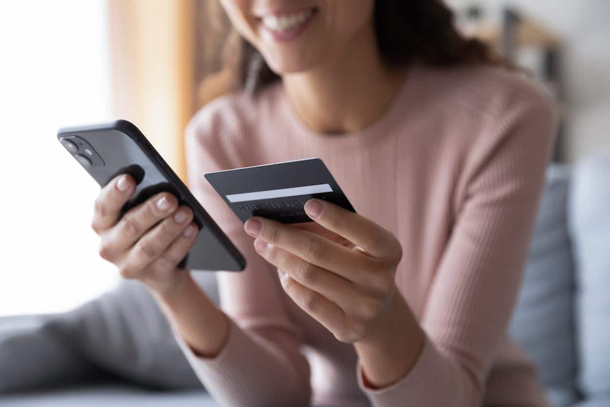 Mulher sorrindo, segundando celular e cartão de crédito