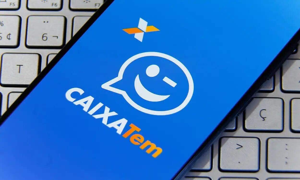 Celular com a tela inicial do aplicativo Caixa Tem, sobre um teclado de notebook. cartão