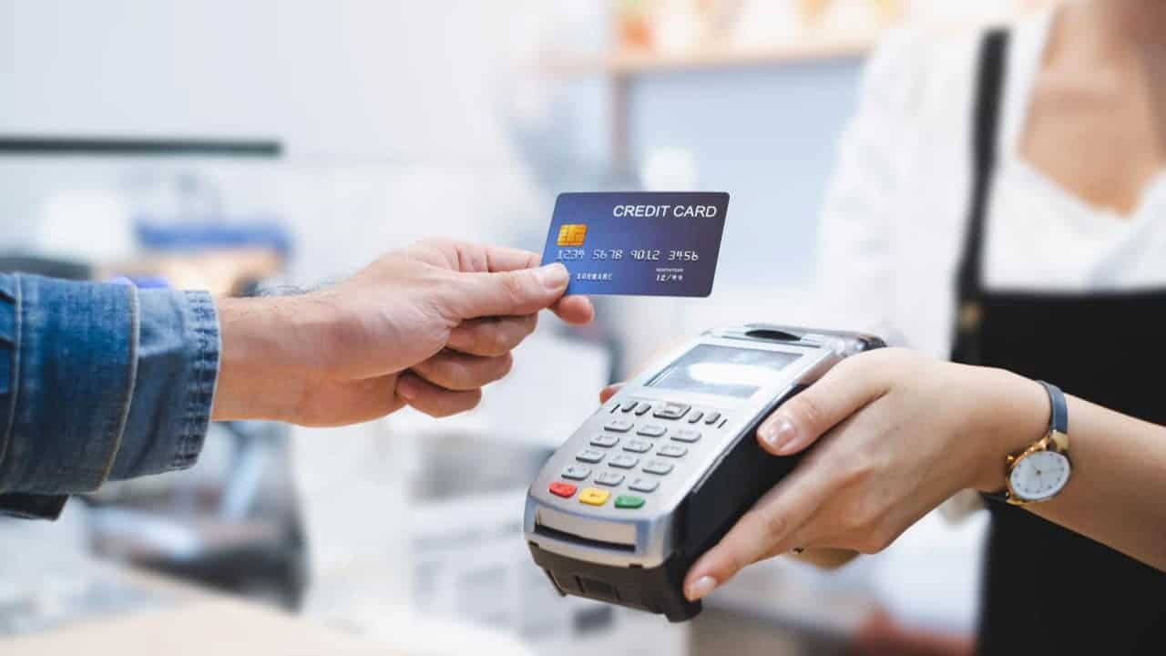 Pessoa segurando cartão de crédito e outra segurando maquininha de cartão bc