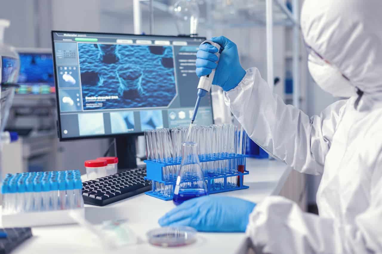 Cientista vestido com roupas de proteção, trabalhando em um laboratório com um monitor à frente.