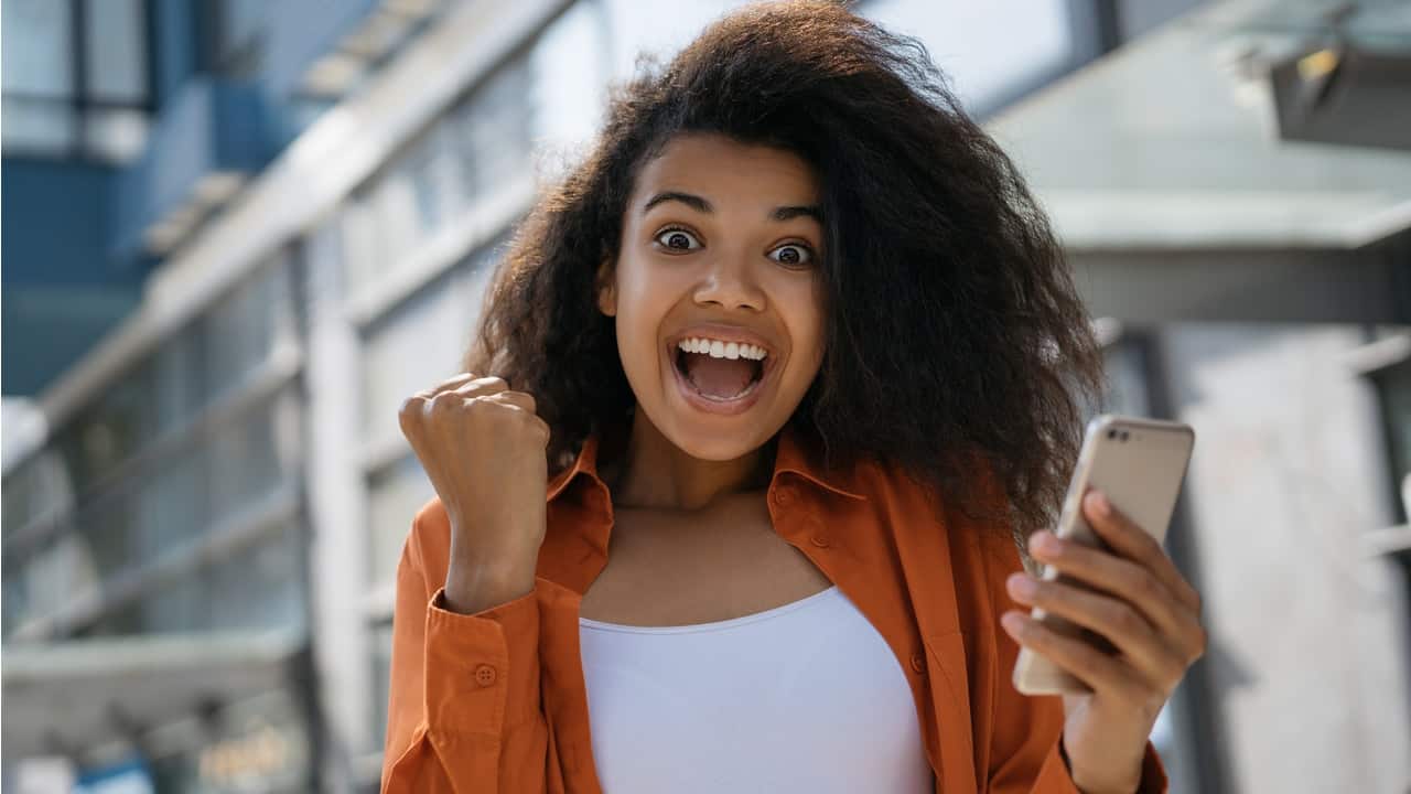 Moça jovem comenorando novo auxílio com celular na mão