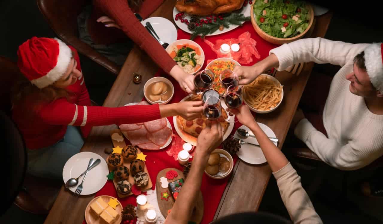 Imagem mostra 5 pessoas de uma família brindando sentadas à mesa em uma ceia de Natal