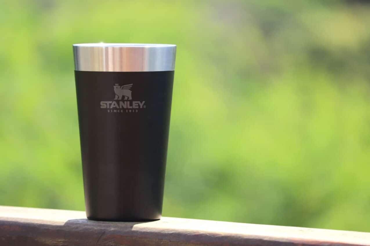 Copo preto da marca Stanley sobre uma superfície de madeira. Fundo verde e desfocado.