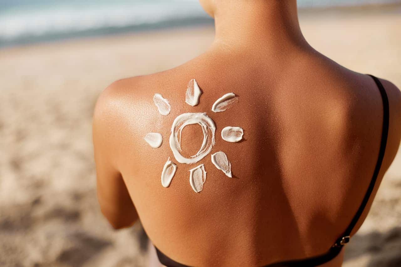 mulher na praia de costas. do lado direito das costas um sol desenhado de protetor solar