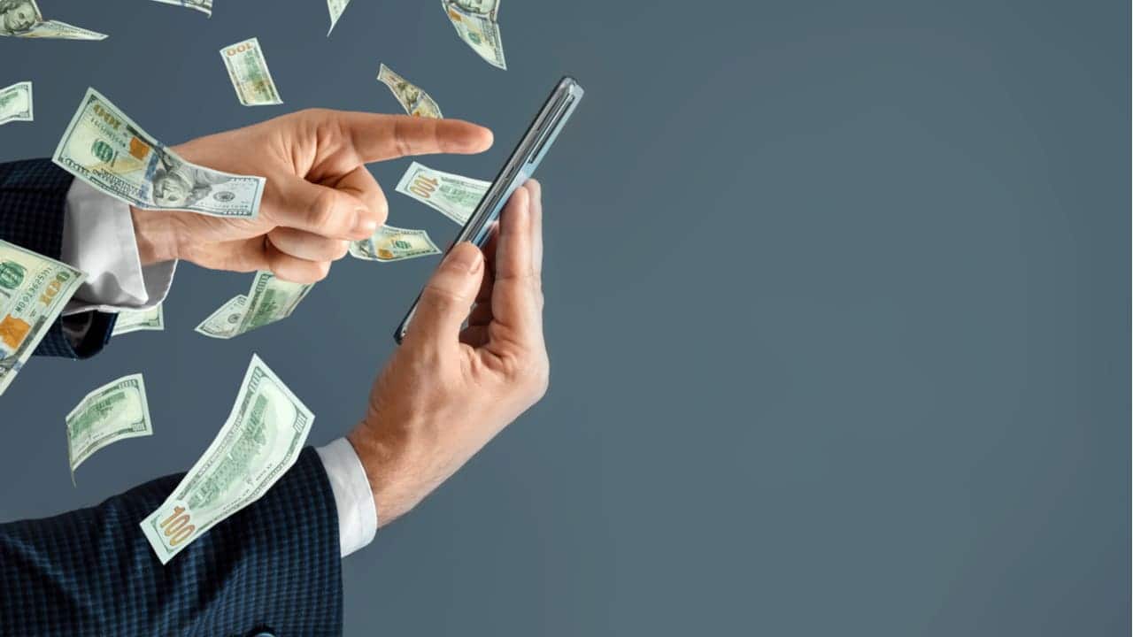Mão segurando celular que tem várias cédulas saindo
