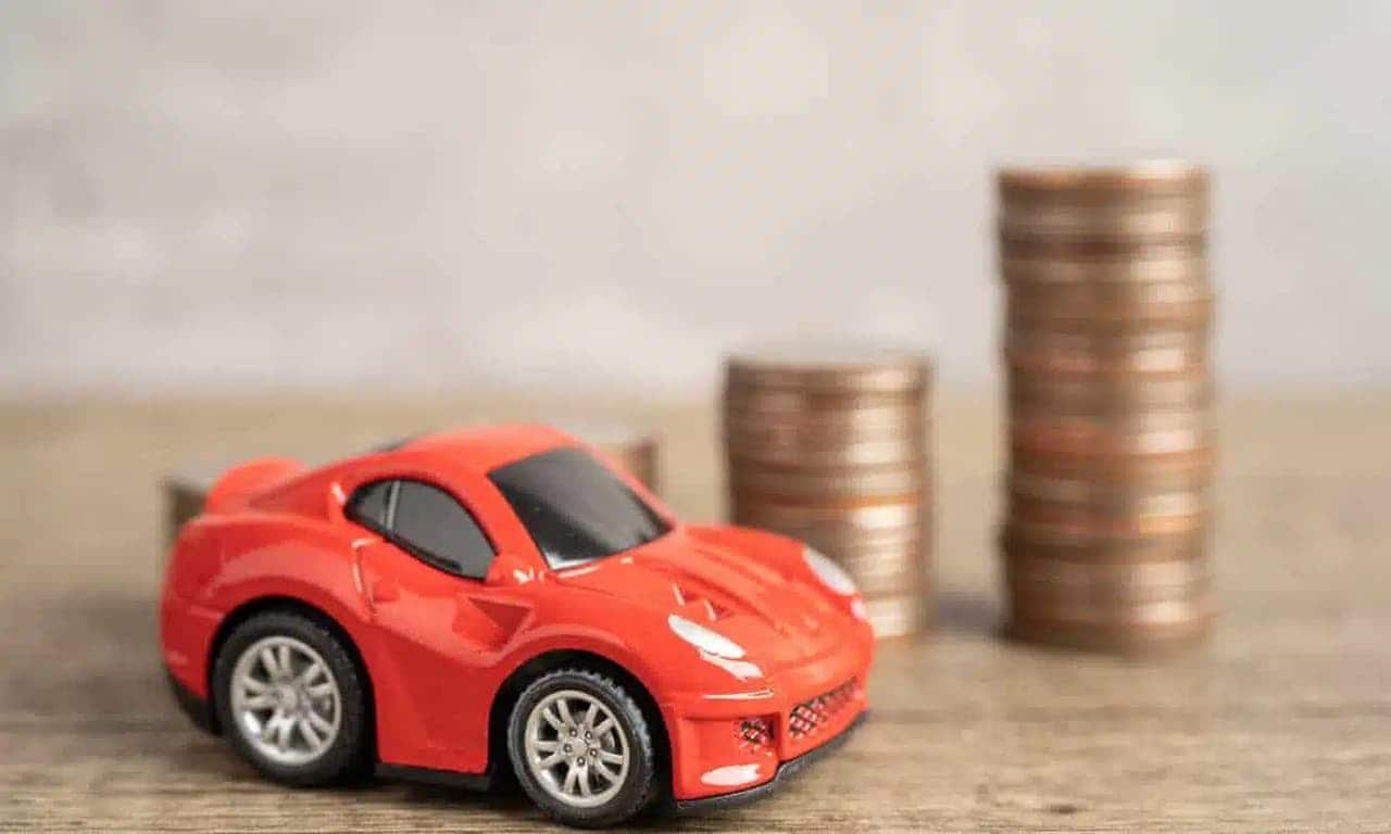 Miniatura de carro vermelho e duas pilhas de moedas