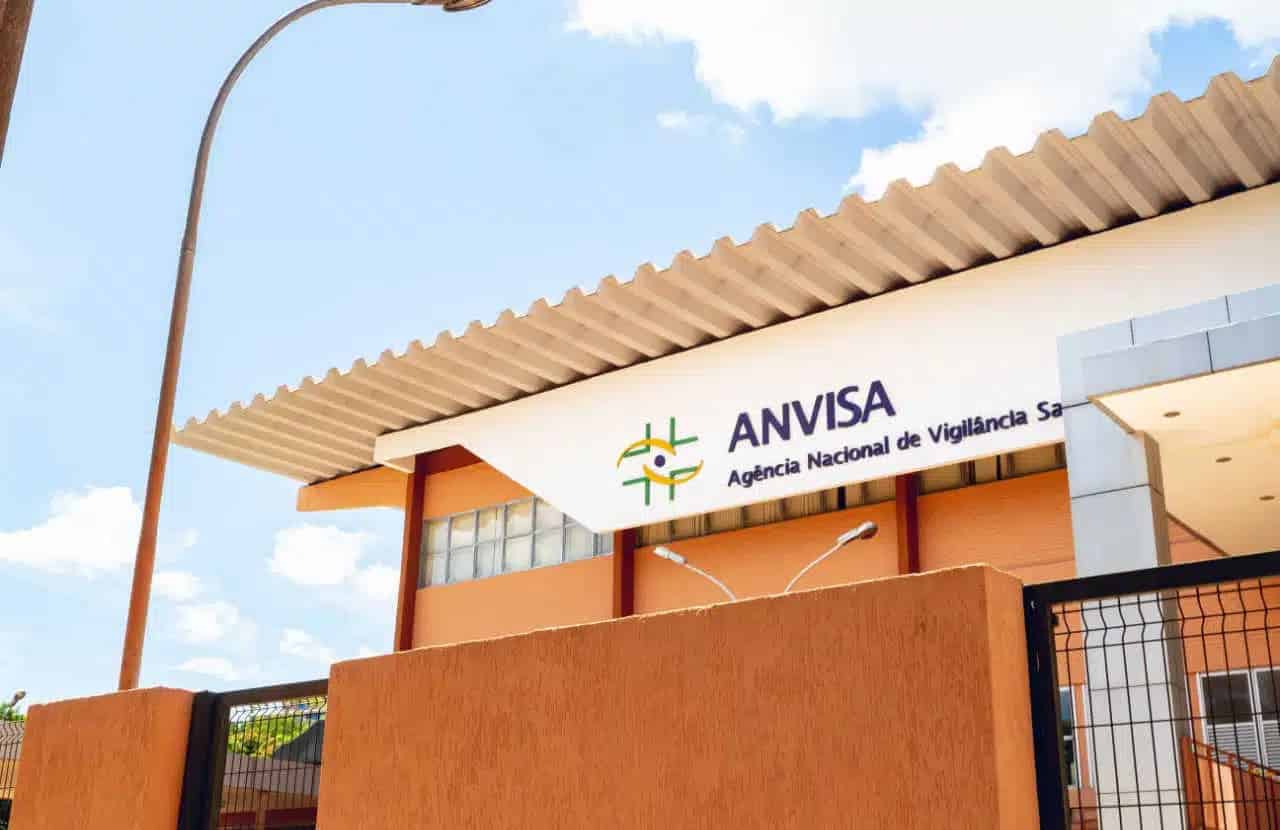 Fachada de prédio da Anvisa. O prédio é de tom terroso e a parte em que fica o logo e nome é branca