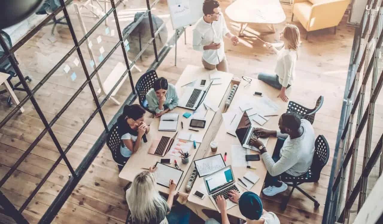 Grande sala de coworking com diversas pessoas trabalhando em volta de mesas com computadores