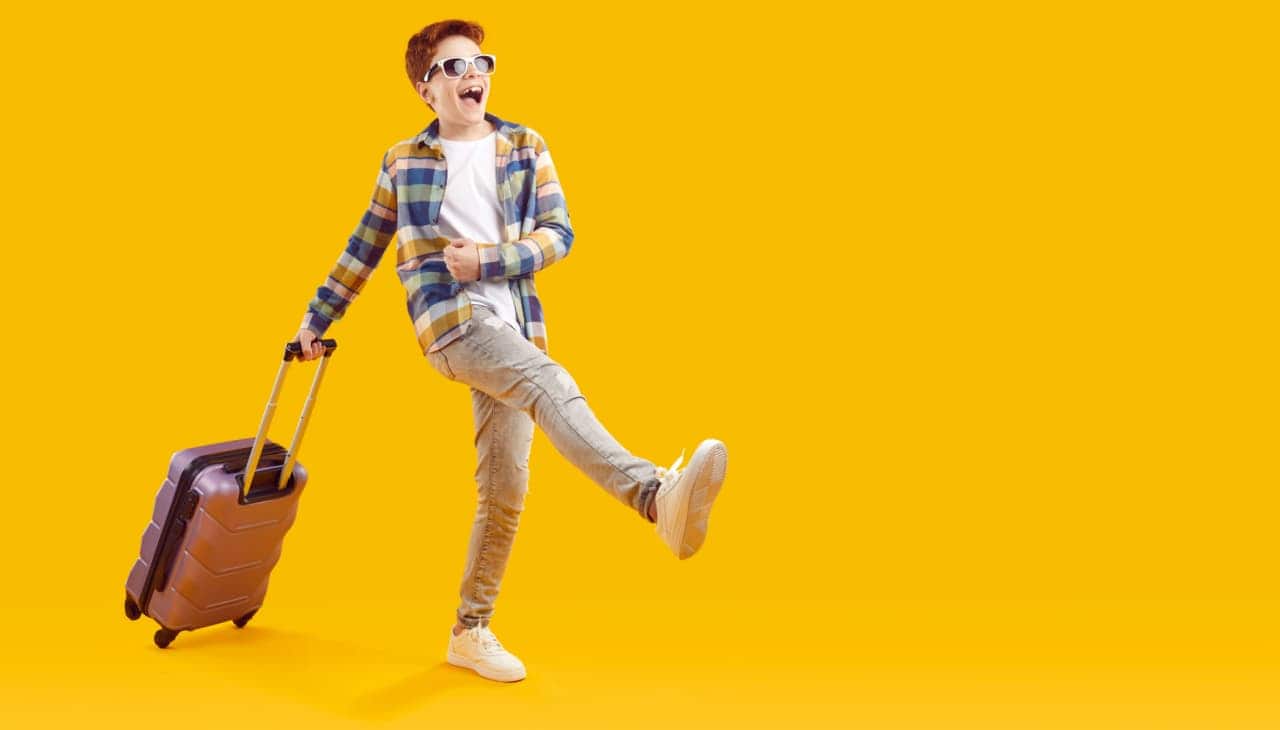 Menino jovem sorrindo e carregando mala para viajar