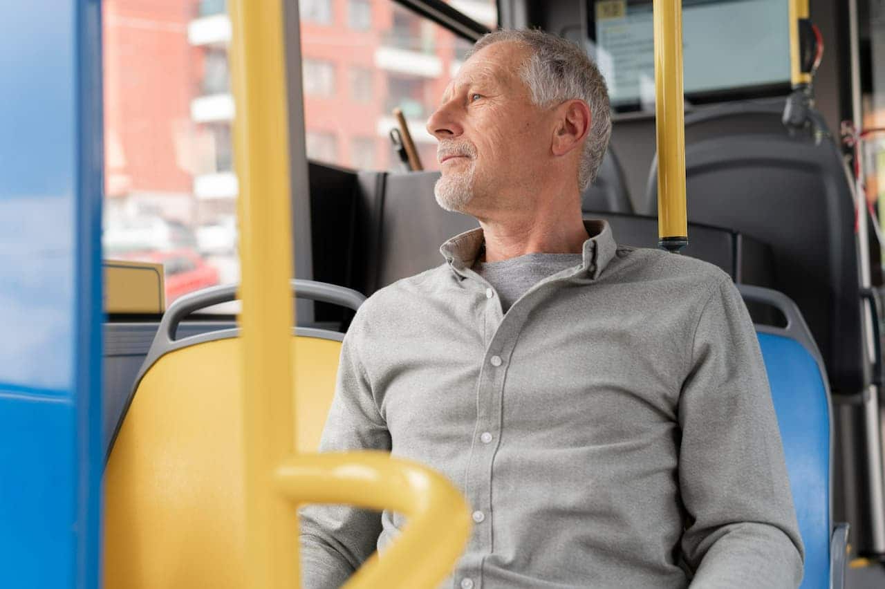 Homem idoso sentado em banco dentro de um ônibus do transporte público.