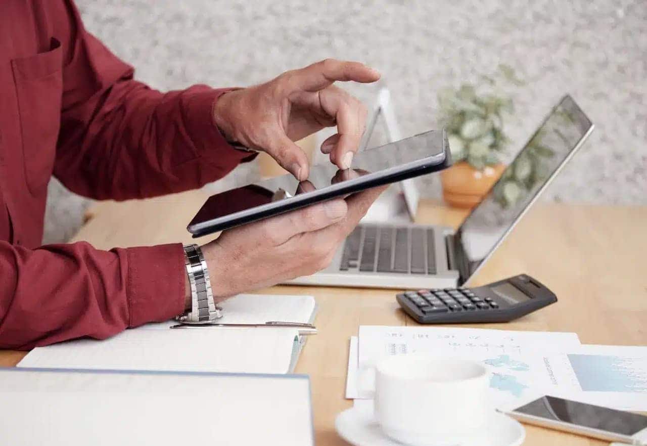 Homem mexendo no tablet em cima de uma mesa com papeis