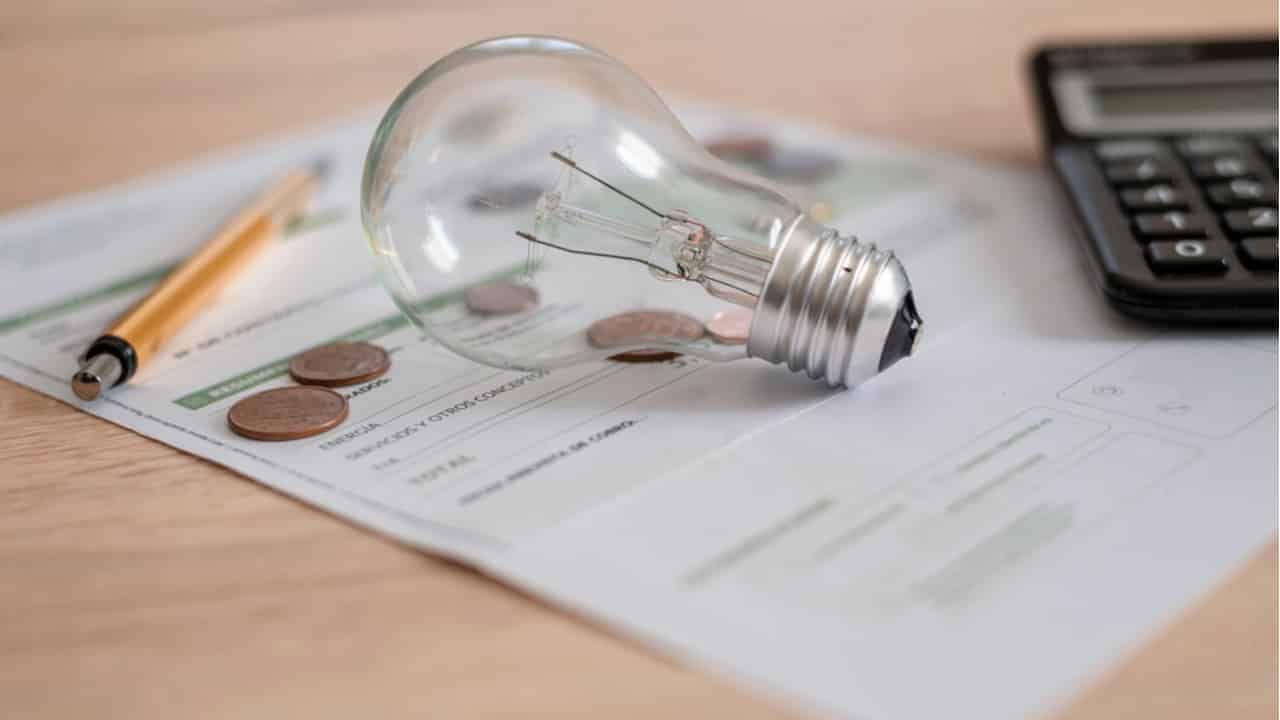 Lâmpada, caneta, calculadora e duas moedas sobre uma conta de luz.