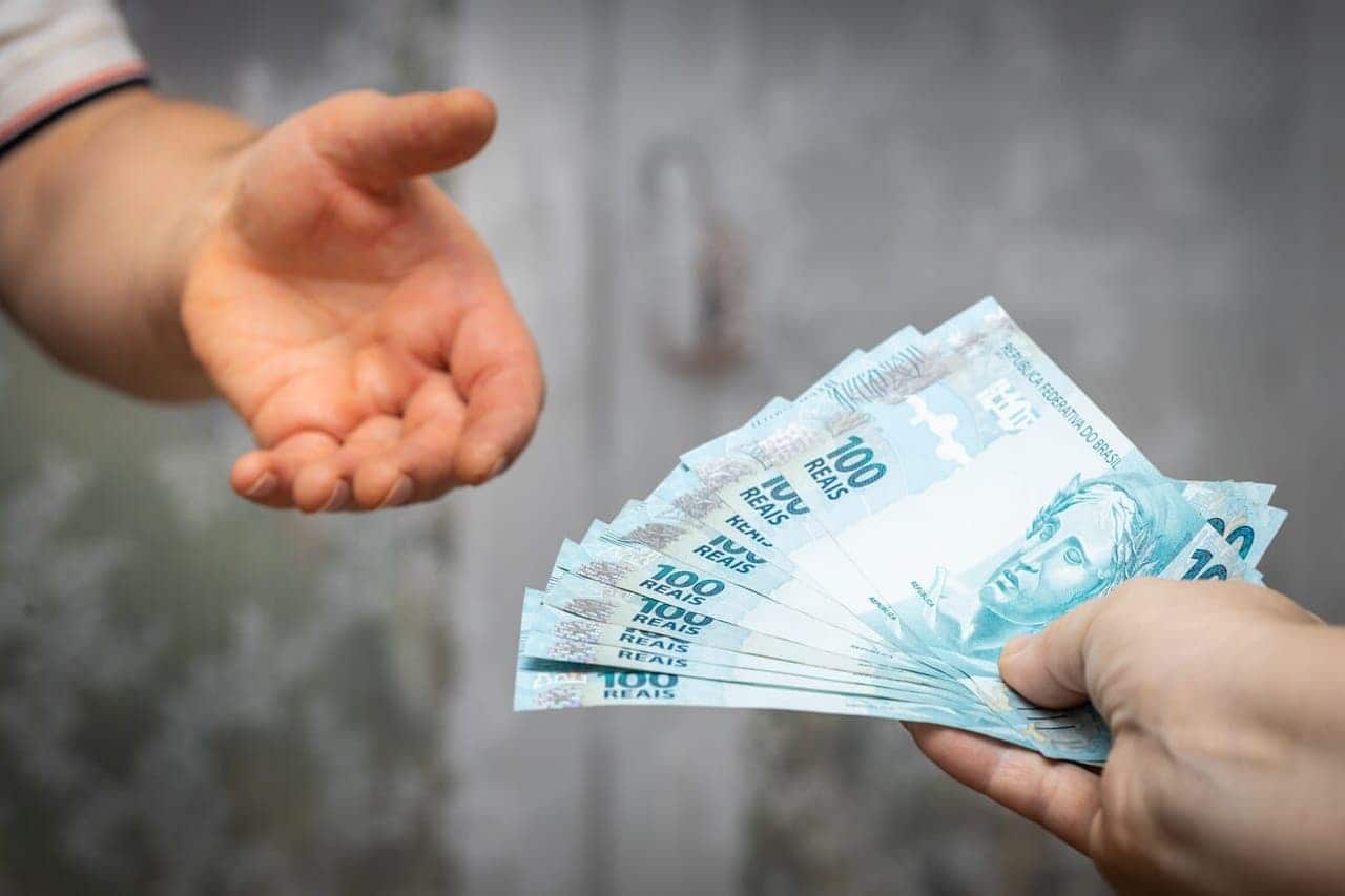 Pessoa com a mão esticada em direção de notas de 100 reais, ilustrando o conceito de empréstimo consignado